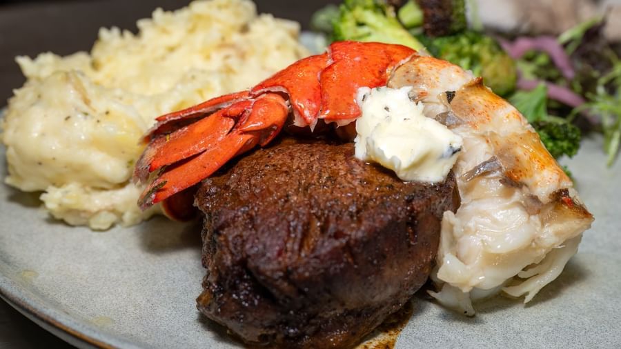 Surf and turf dish at Narrow Gauge Inn with steak, lobster tail, mashed potatoes, and fresh greens.