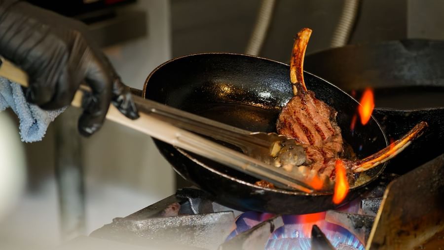 Chef at Narrow Gauge Inn grills bone-in meat over open flame in a hot skillet as part of a freshly prepared dish.