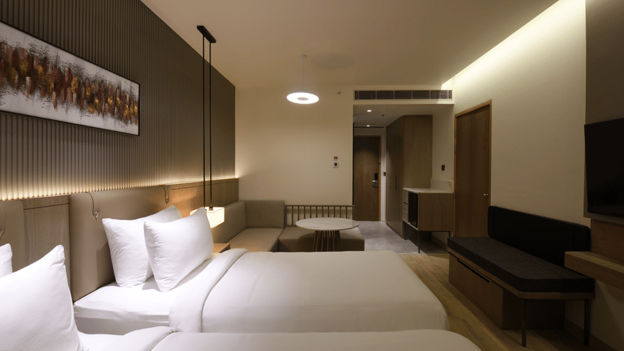 Warmly lit twin-bed room with plush white pillows, a padded headboard, wooden accents, and a decorative artwork panel above the beds.