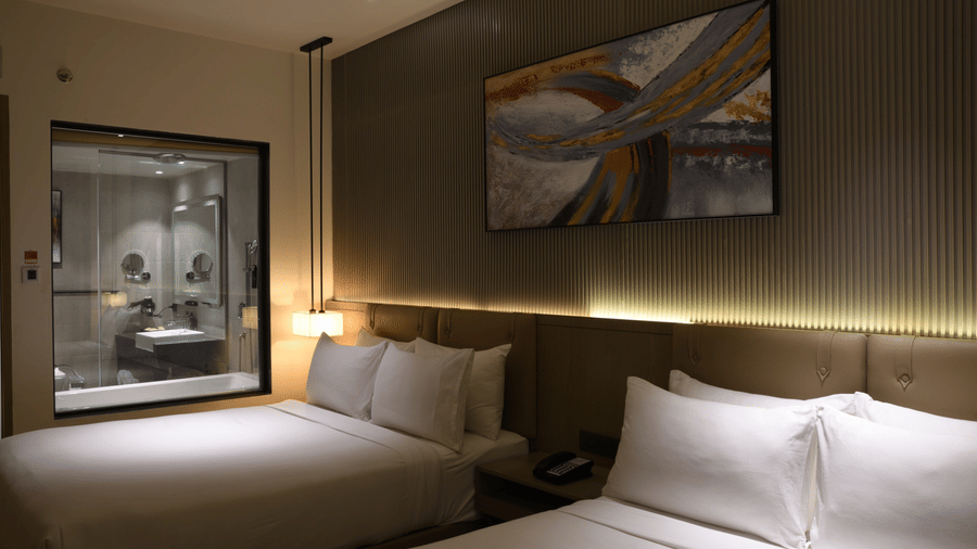 Dimly lit, cosy hotel room at Ramada by Wyndham Sonipat Murthal, with a king size bed, white linens, warm wooden accents, and a large framed artwork on the wall.