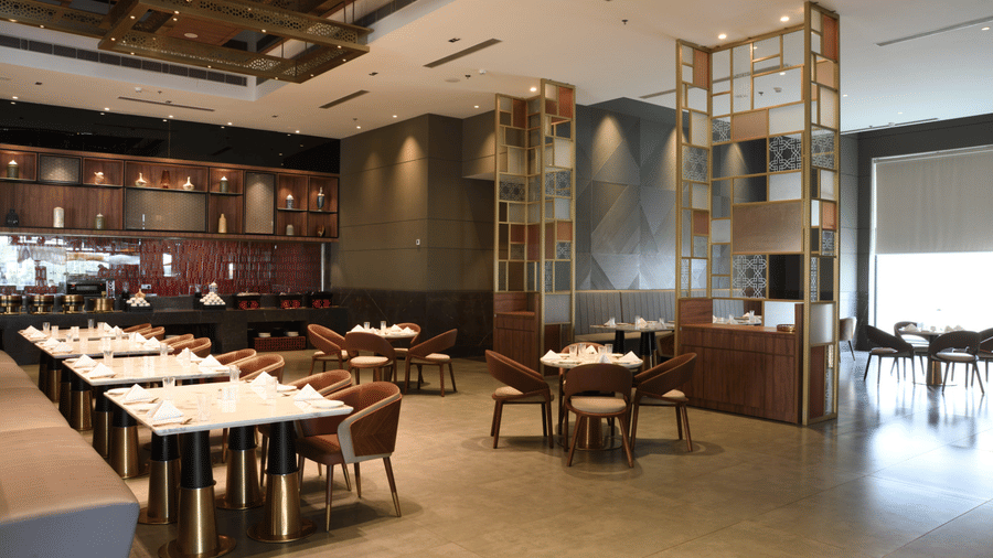 Elegantly set dining area at Ramada by Wyndham Sonipat Murthal, featuring gold lattice partitions, long white-clothed tables, and warm ambient lighting.