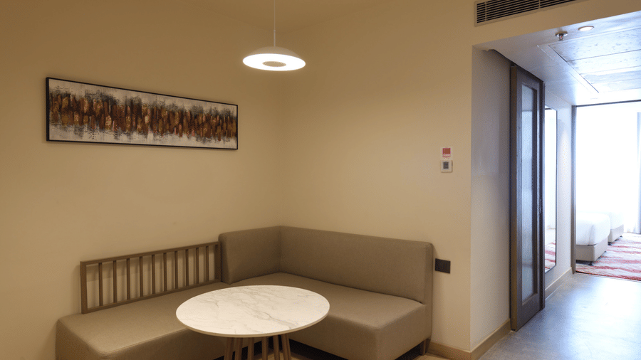 Compact hotel room sitting area at Ramada by Wyndham Sonipat Murthal, with a beige sofa, a round coffee table, and a large window overlooking the outdoors.