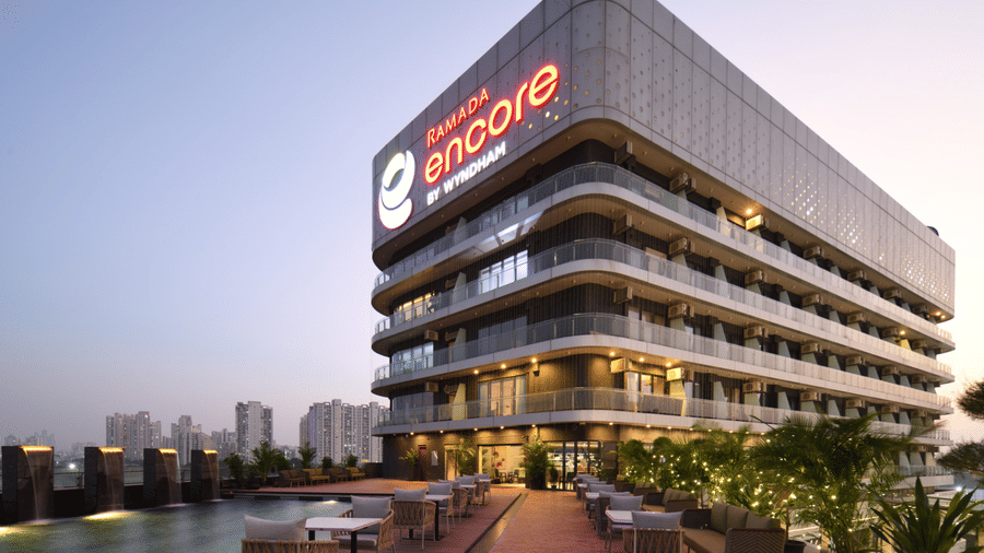 Facade of Ramada Encore by Wyndham Gurugram Dwarka Expressway featuring contemporary architecture, outdoor seating and a pool with a deck.