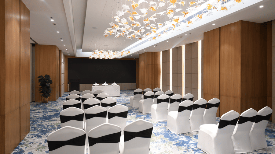 Banquet hall featuring theatre-style seating, aisle layout, stage table, and decorative ceiling installation | Ramada Encore by Wyndham Gurugram Dwarka Expressway