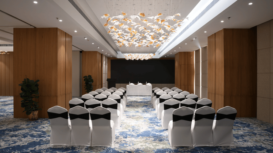 Conference hall arranged in theatre style with rows of chairs, a stage table, and elegant ceiling decor | Ramada Encore by Wyndham Gurugram Dwarka Expressway