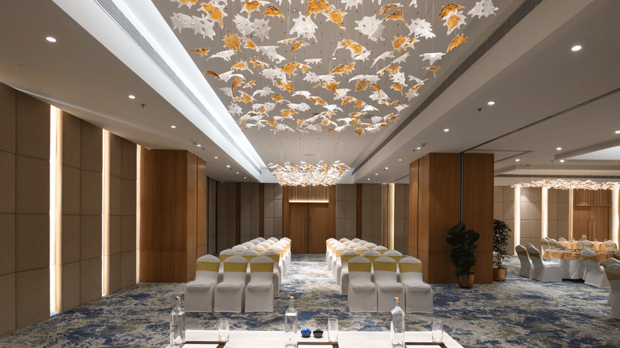 Elegant banquet hall with theatre-style seating, a presentation table, and decorative ceiling installation | Ramada Encore by Wyndham Gurugram Dwarka Expressway