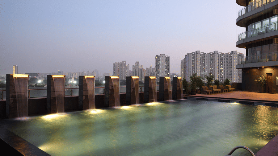Illuminated rooftop infinity pool offering elevated city views at dusk | Ramada Encore by Wyndham Gurugram Dwarka Expressway