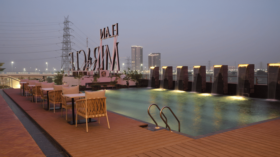 Rooftop infinity pool with deck seating and panoramic city skyline views | Ramada Encore by Wyndham Gurugram Dwarka Expressway