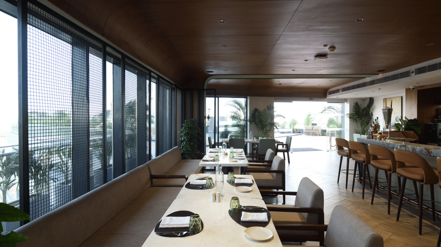 Modern dining room with neatly set tables, wood-panelled ceilings, and large windows | Ramada Encore by Wyndham Gurugram Dwarka Expressway