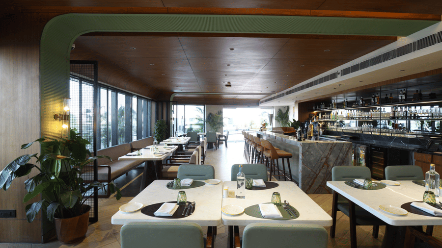 Dining area of a restaurant featuring neatly set tables, mint-green chairs, and a sleek bar area with a wood-panelled ceiling | Ramada Encore by Wyndham Gurugram Dwarka Expressway