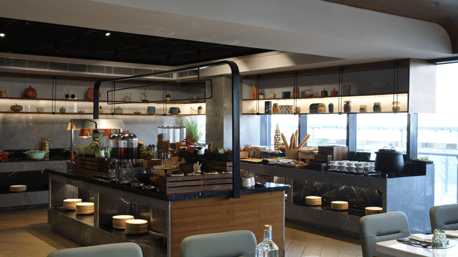 A breakfast station with marble counters, featuring tiered displays of fresh pastries, breads, and cereals under warm lighting | Ramada Encore by Wyndham Gurugram Dwarka Expressway