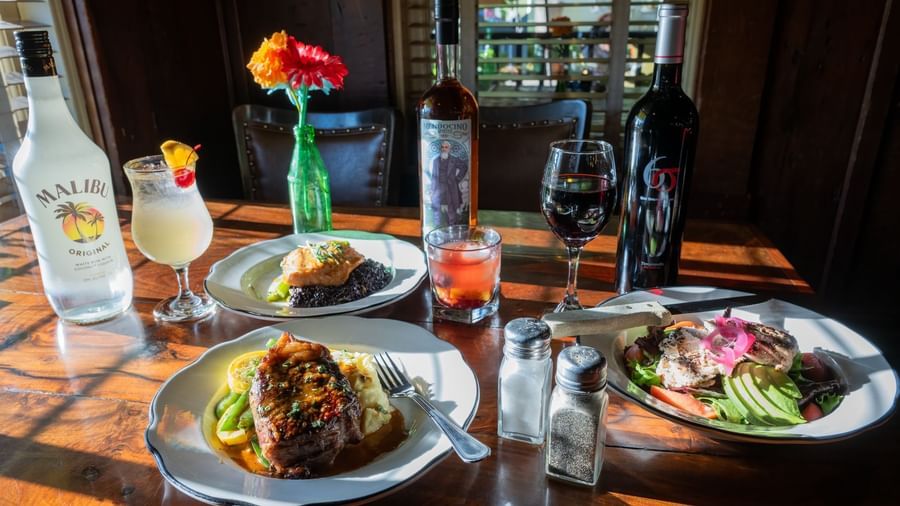 Three plates of food placed on a table at Tallman Hotel alongside bottles of beverage, floral decor and seasoning shakers.