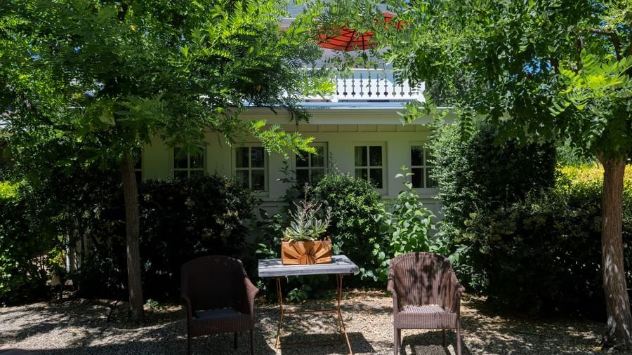 A view of garden seating area at Tallman Hotel with chairs and tables under the trees with a small white cottage in the back.