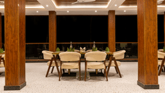 An outdoor dining table set up on a patio with wood columns, soft chairs, and a dark night background.