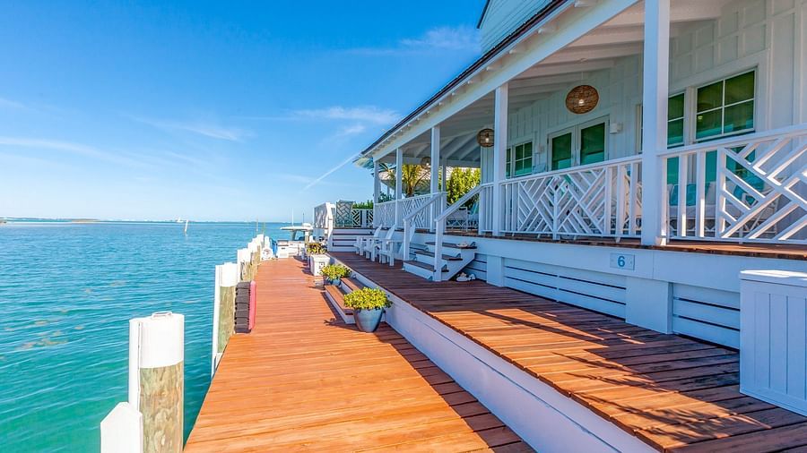 Waterfront wooden deck alongside a white coastal cottage with seating, overlooking calm blue sea under a clear sunny sky at Abaco Inn