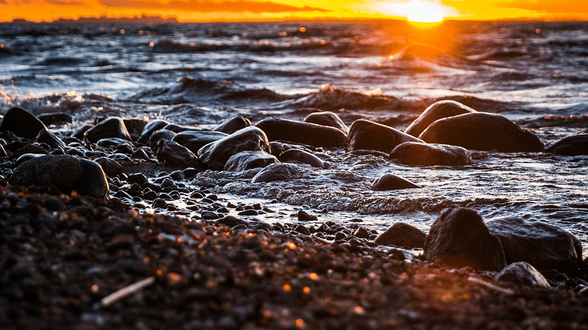 a view of rocks on a water body at sunset 