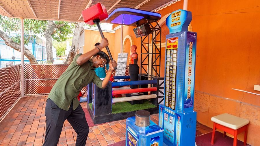 Visitor playing a high striker hammer game at MGM Dizzee World, preparing to hit with a large red mallet in a vibrant arcade setting.