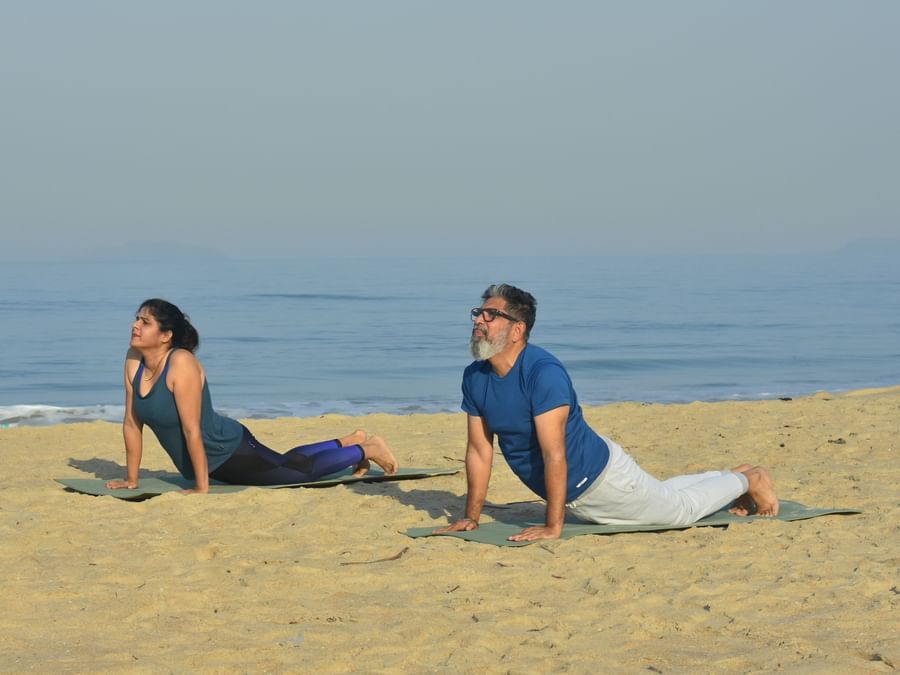 A couple performing Yoga on the beach with the sea in the background - Heritage Village Resort & Spa, Goa
