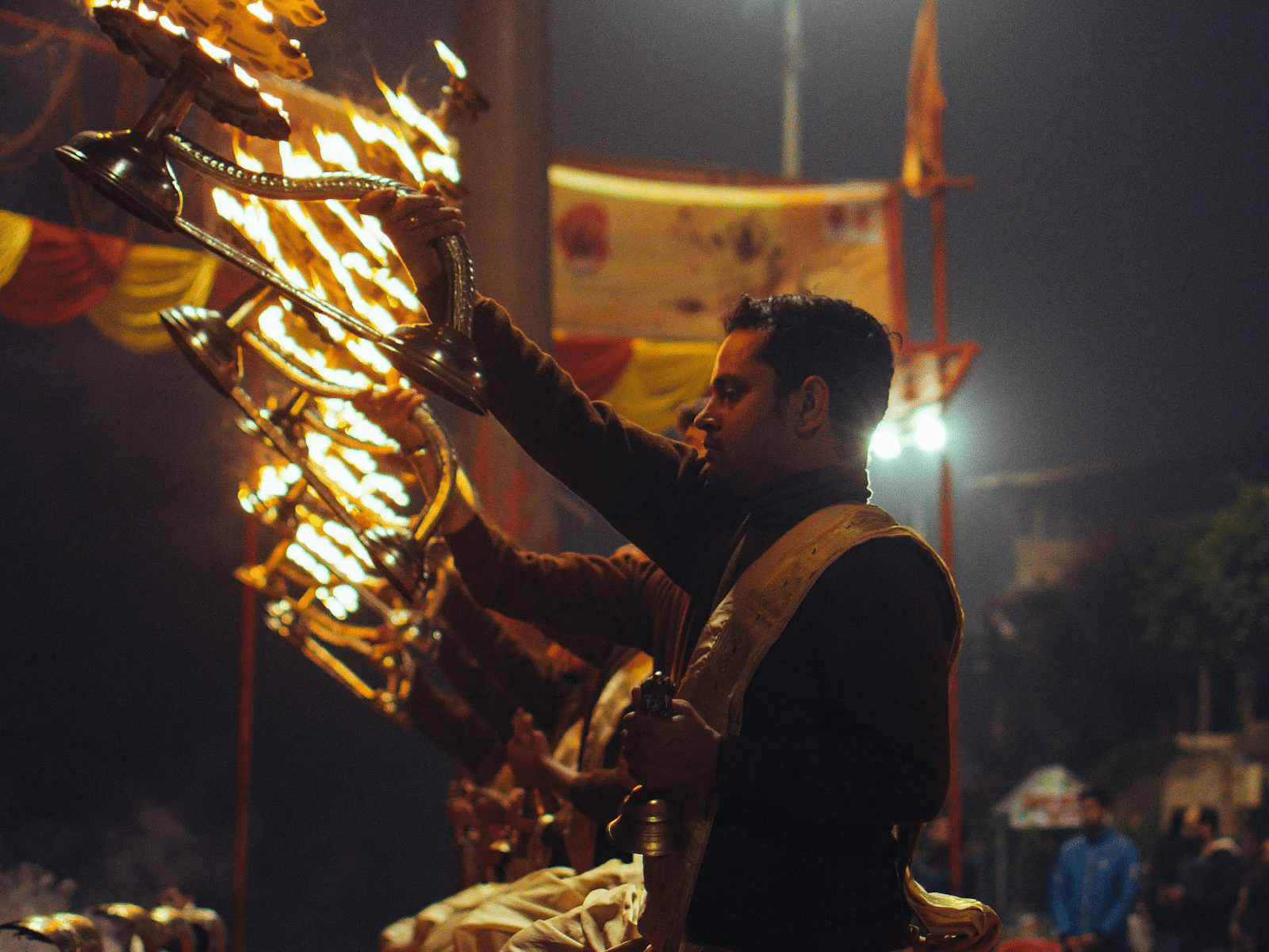 A priest performing Ganga Aarti with multiple lit oil lamps at night.