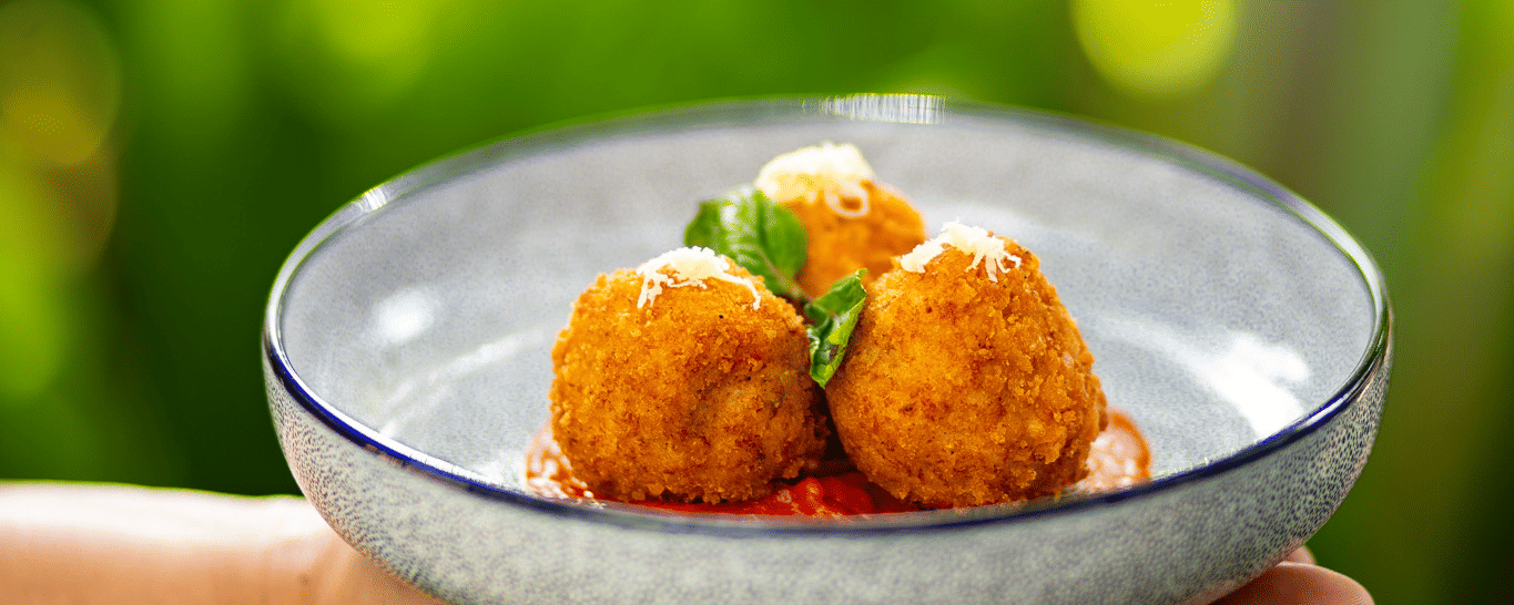 A person holds a plate with three fried, golden-brown appetisers on a bed of red sauce at Stanley Revelation.