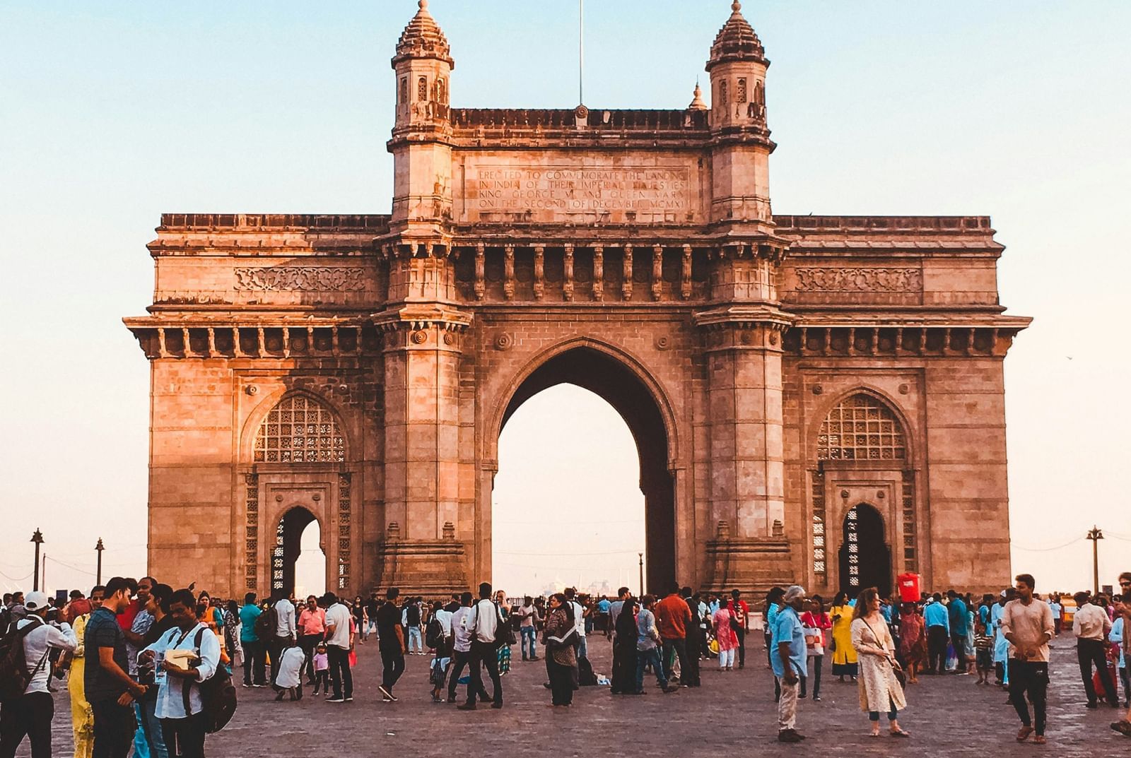 The Gateway of India monument in Mumbai with people standing in front of it on a bright day.