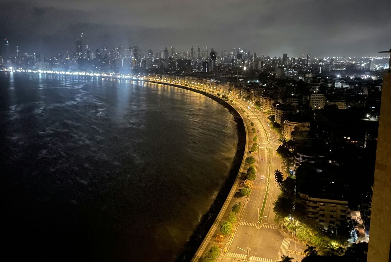 An aerial night view of a brightly lit waterfront road curving along a coastline.