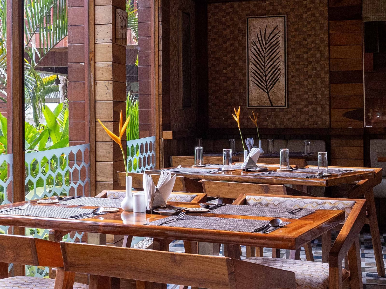 A spacious dining area at Ocean Prime with wooden tables and chairs, set in a modern wooden room. The decor is minimalist, with large windows offering a glimpse of the outside greenery - Coral Reef Resort & Spa, Havelock