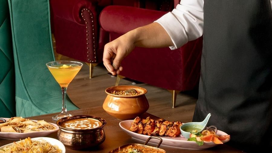 A chef at Clarks Inn, Basti, garnishes a dish on a table with a variety of food and drinks in a restaurant setting.