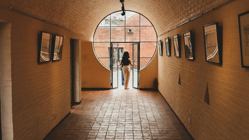 hallway with frames put up on both walls and a person moving out through the hallway door