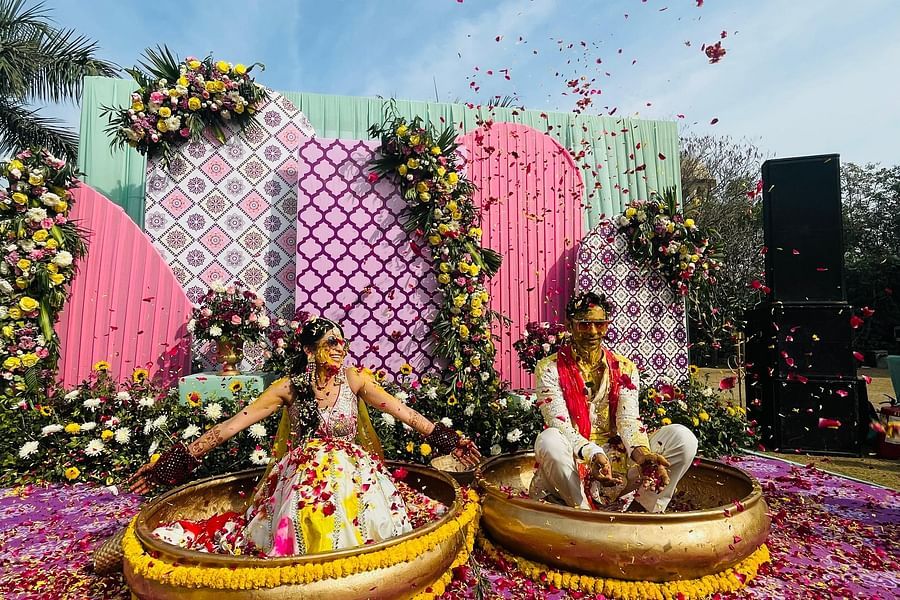 a bride and groom sitting on big bowls during haldi ritual with rose petals placed around them - heritage village resorts & spa, Manesar