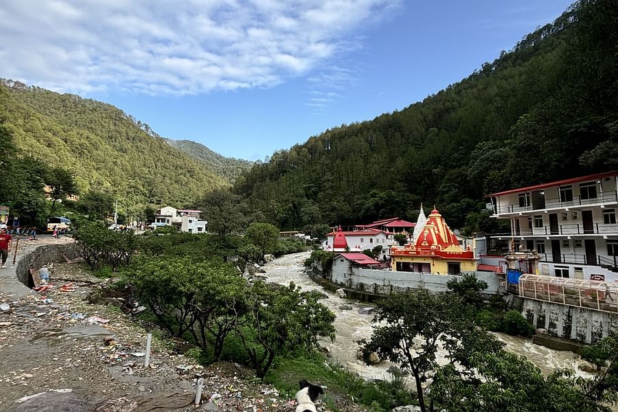 A view of a temple nestled in a valley surrounded by mountains,flowing river, with a clear blue sky and fluffy clouds.