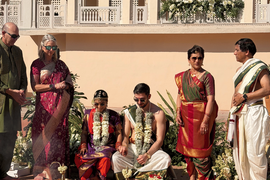 A family gathered together outdoors in a courtyard at Umaid Palace performing traditional Hindu wedding ceremony rituals on the ground.