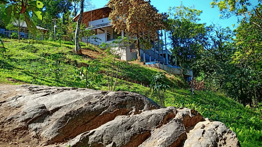 A house perched on a slope, surrounded by trees and large rock formations.- Abad Brookside Lakkidi, Wayanad