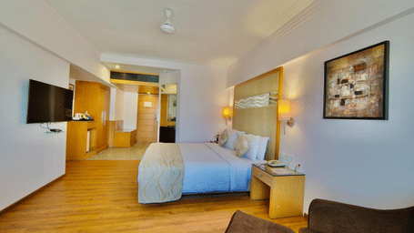 Spacious bedroom in Lords Plaza Ankleshwar featuring a double bed, T.V., and a lounge chair, highlighting its modern interiors.