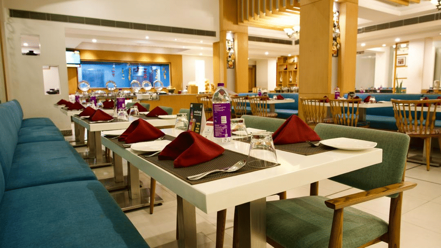 A well lit dining area of Lords Plaza Ankleshwar with buffet stations and neatly arranged tables and chairs 