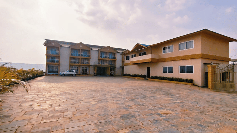 Multi-storey resort buildings stand beside a spacious paved stone driveway under a lightly clouded sky at Savyasaachii Hotel.