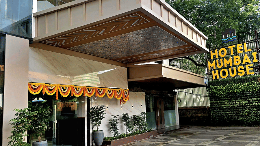 Exterior entrance of Hotel Mumbai House, Thane, featuring marigold garland decorations, green foliage, and illuminated hotel signage.