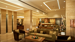 An image of a reception lobby featuring sofa sets, centre table, reception desks, and a few people standing at Adarsh Hamilton