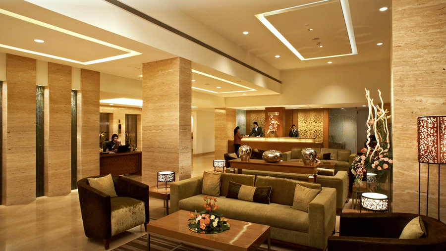 The well-lit lobby at Adarsh Hamilton, with cushions, tables, and decorated ceiling.