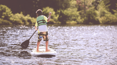 A boy balancing on a surf board and kayaking through the water