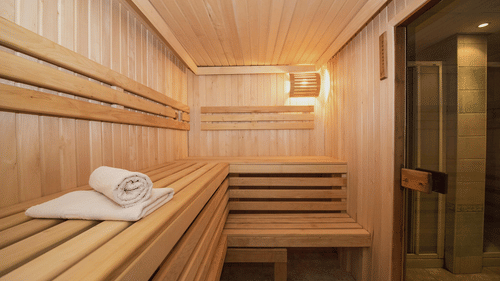 A wooden sauna room with benches, a towel, and a light fixture at the best resort in Bangalore.