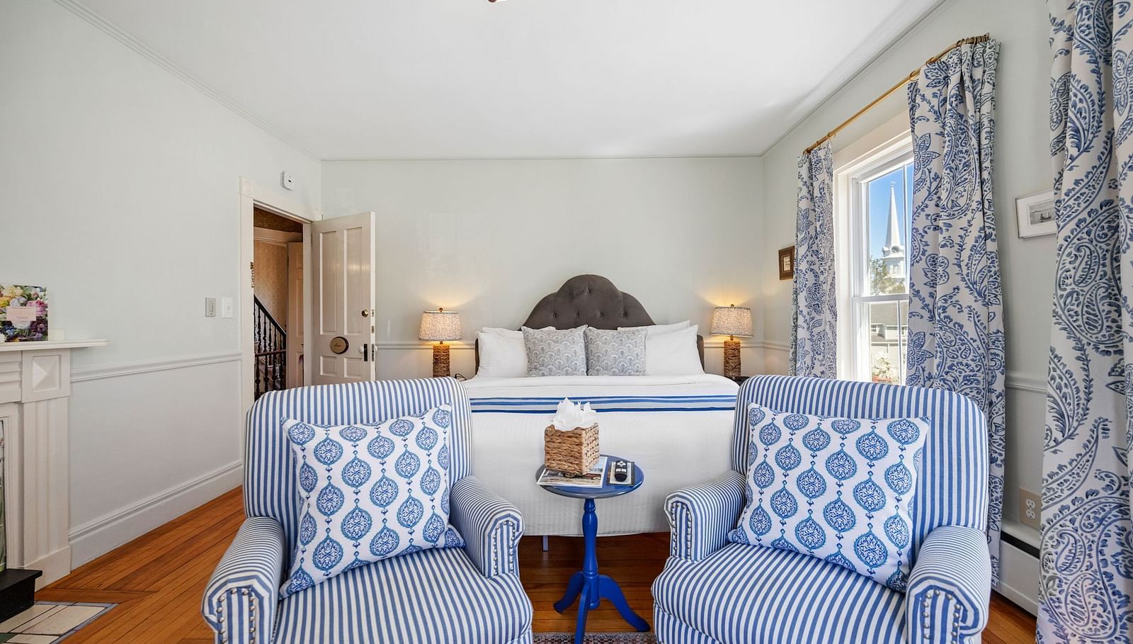 Seating area with blue patterned chairs, round table and showcasing queen sized bed in the background at Hartstone Inn