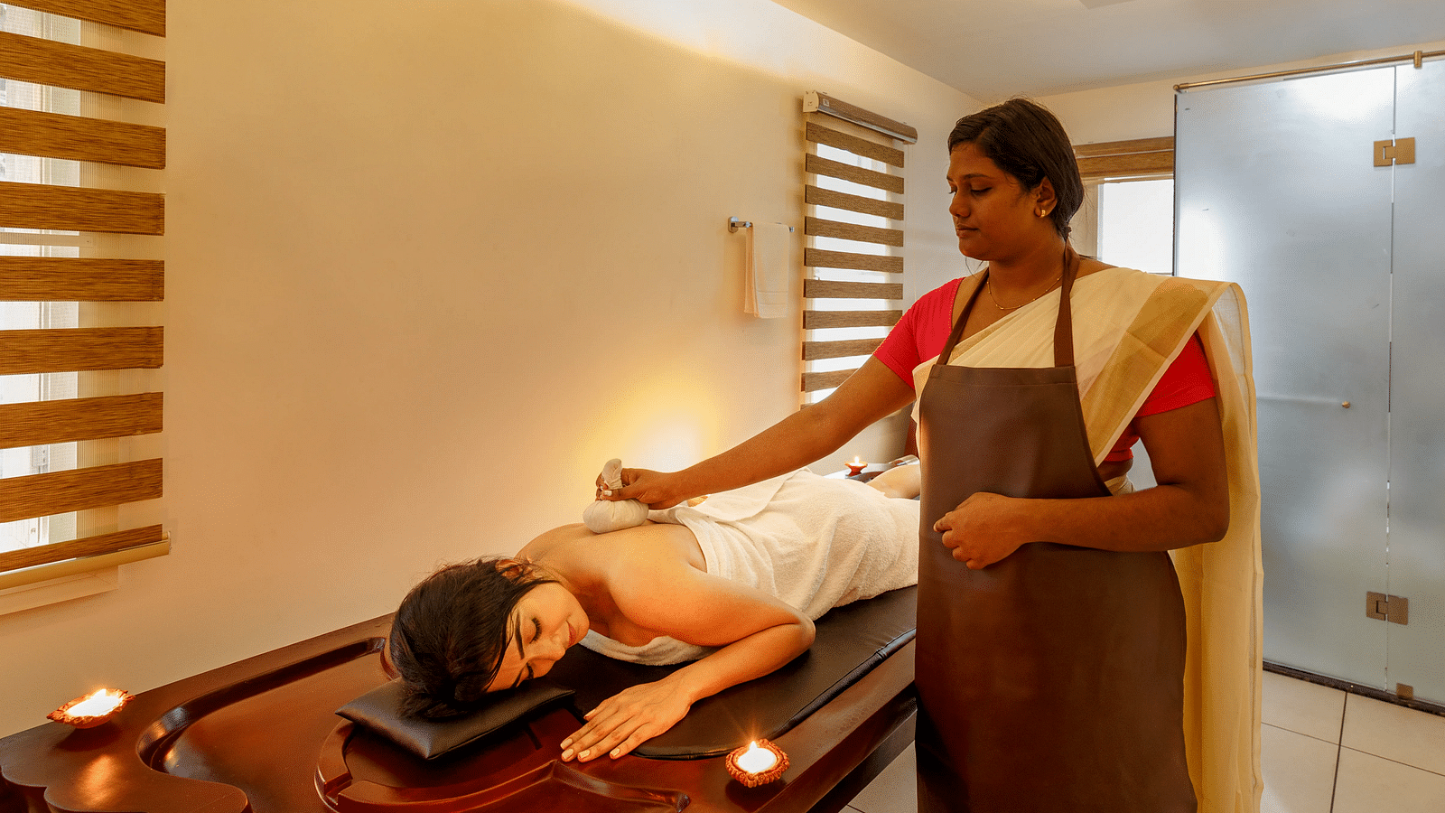 A person receiving a massage treatment on a wooden table in a softly lit room with brick accents.