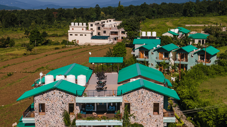 Multiple buildings of Corbett Nirvana Resort, Uttarakhand featuring cottage style facades  in cluster surrounded by lawns.