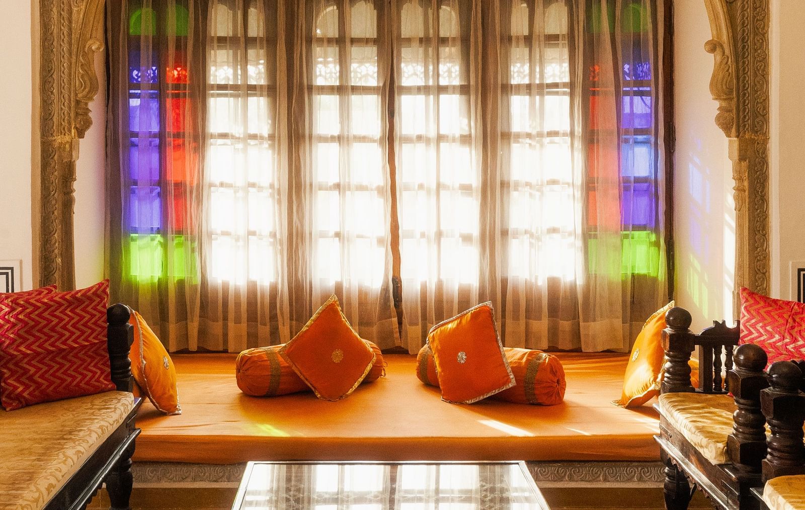 A cosy alcove at Fort Barli, featuring stained glass windows, plush cushions, and a low table, creates a vibrant and inviting seating area.