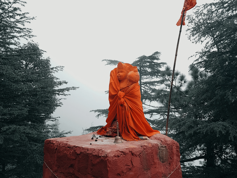 An idol of Lord Hanuman with a religious flag next to it on a hilltop