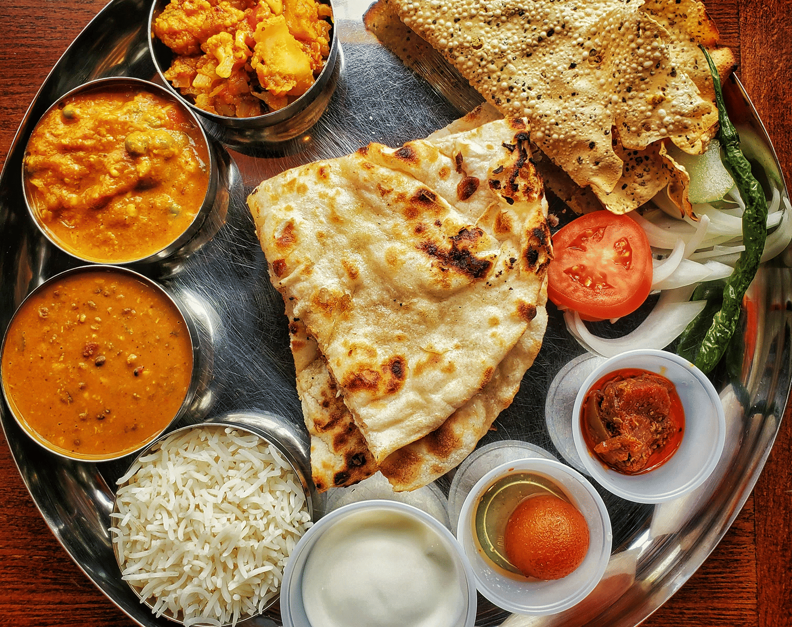 A neatly arranged plate with several Indian delicacies served.