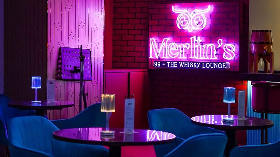 blue chairs and wooden table placed on a marbled floor with merlin's 99 signboard glowing in pink in the background