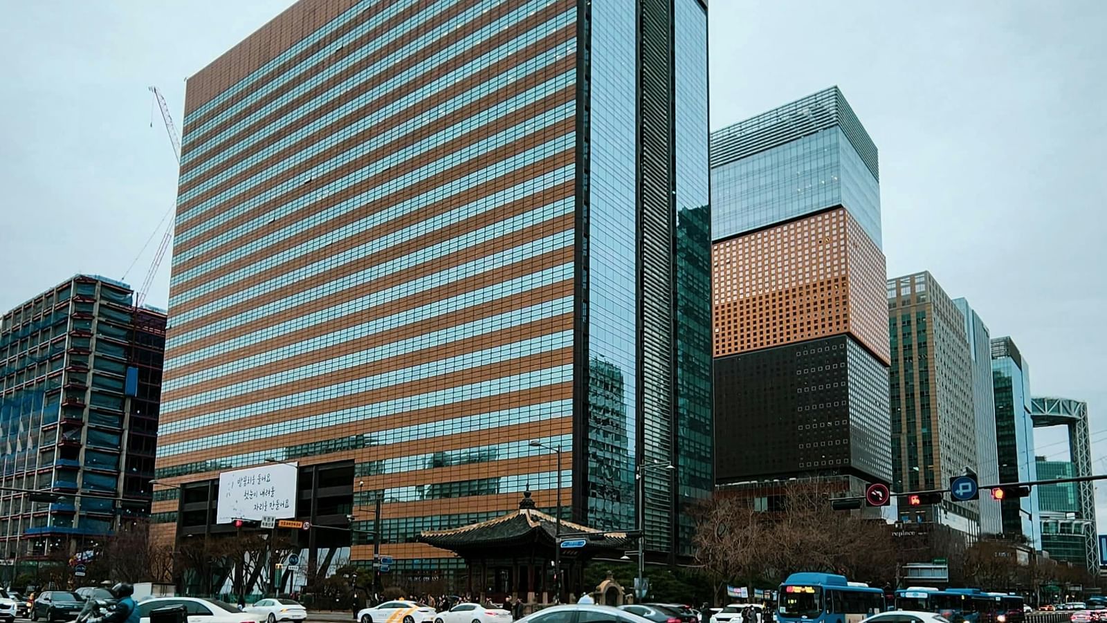 A bustling street scene in a modern city with a large brown skyscraper, a pedestrian crossing, and traffic.