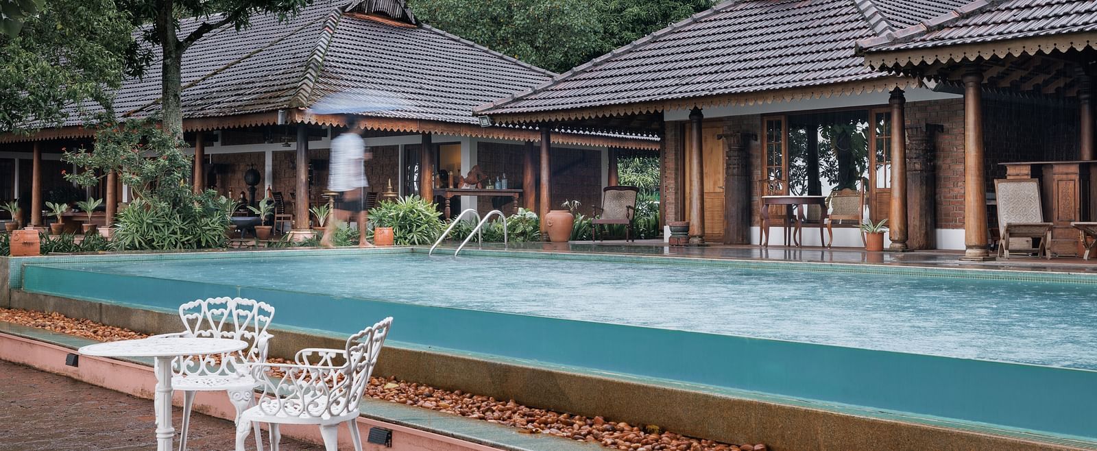A shot of the pool with chairs and table near it and the restaurant in the background - BluSalzz Villas - Muhamma Resort, Alleppey